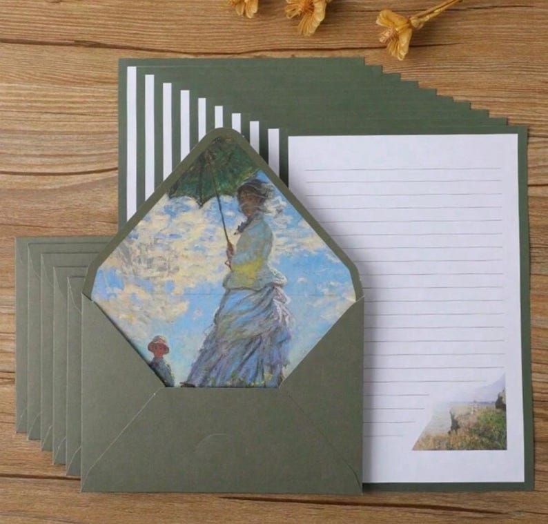 Pu&ograve; includere: Un set di cartoleria verde con carta bianca rigata e buste. Le buste hanno una finestra che mostra un dipinto di una donna con un ombrello.