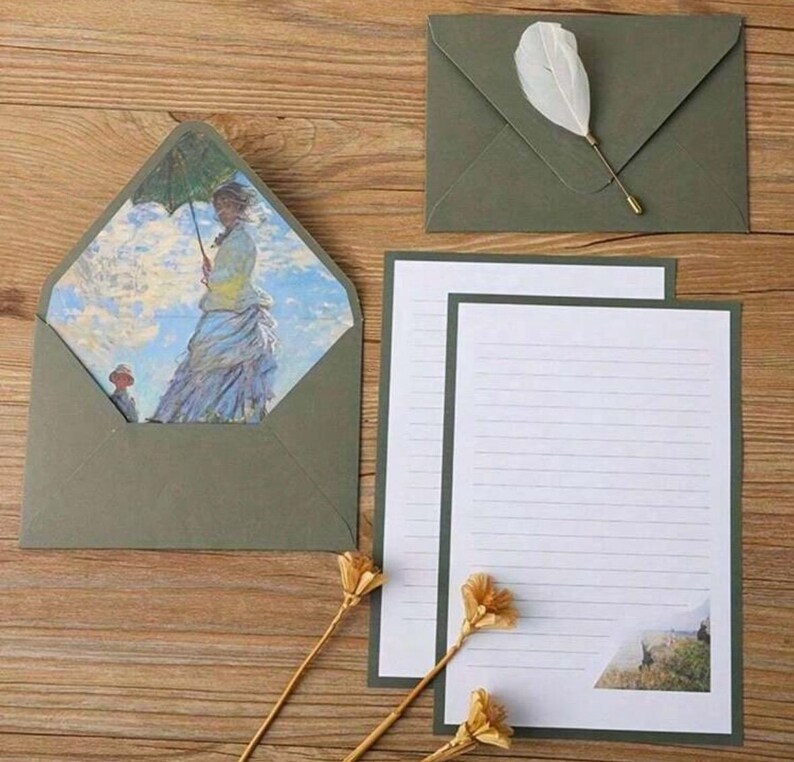 Pu&ograve; includere: Un set di cartoleria verde con un foglio di carta rigato e una busta con un dipinto di una donna con un ombrello. La busta ha una patta decorativa.