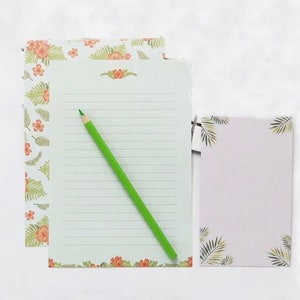 May include: A set of stationery featuring a floral design with green leaves and orange flowers. The set includes a lined sheet of paper, a blank sheet of paper, and a green pencil.