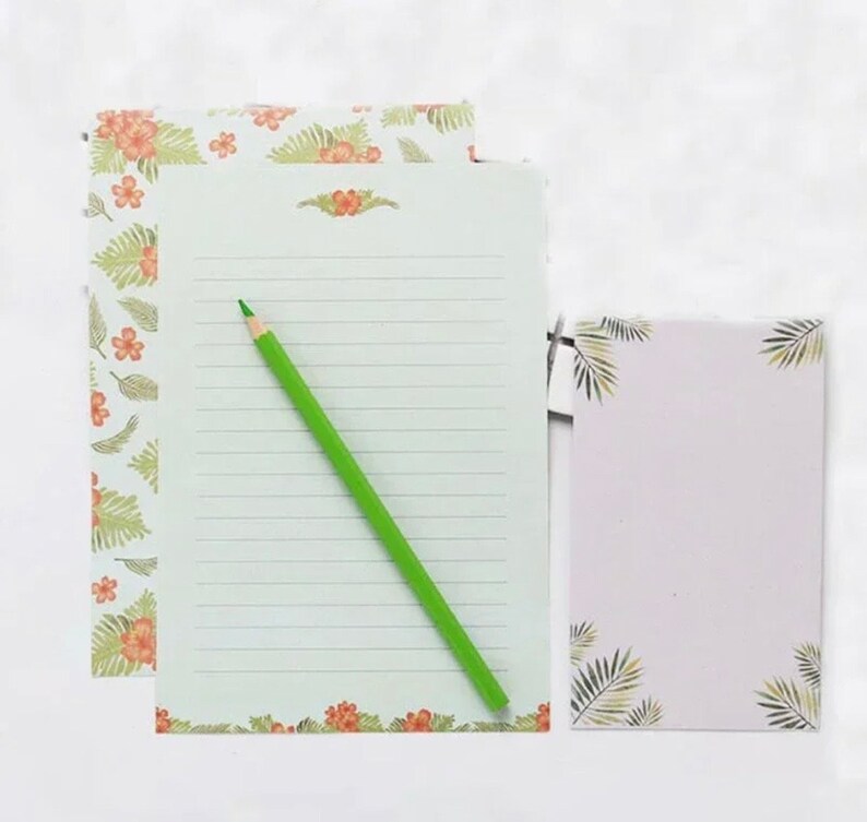 May include: A set of stationery featuring a floral design with green leaves and orange flowers. The set includes a lined sheet of paper, a blank sheet of paper, and a green pencil.