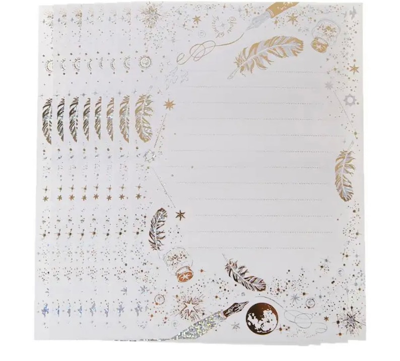 Puede incluir: Una pila de hojas de papeler&iacute;a blancas con un dise&ntilde;o celestial. Las hojas presentan detalles dorados y plateados de plumas, estrellas, lunas y tinteros. P&aacute;ginas rayadas listas para escribir.