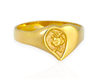 May include: A gold-colored ring with a heart-shaped face. The heart features an embossed floral design. The ring is set against a white background, highlighting its polished finish. The ring is a piece of jewelry.