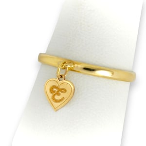 May include: A gold ring with a heart-shaped charm. The charm features the letter "E" in a decorative font. The ring is displayed on a white surface, showcasing its polished finish and design.