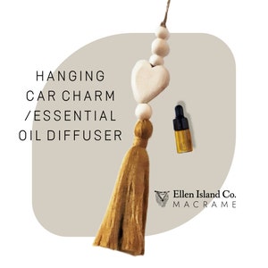 May include: A hanging car charm and essential oil diffuser. The charm includes a wooden heart, beads, and a mustard-coloured tassel. An essential oil bottle with a black cap is also visible. The image text reads "Hanging Car Charm / Essential Oil Diffuser."