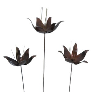 May include: Three metal flowers with brown and rust coloured petals and green stems. The flowers are arranged in a bouquet.