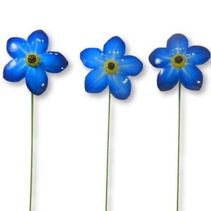 May include: Three blue metal flowers with yellow centres and green stems. The flowers are arranged in a row.