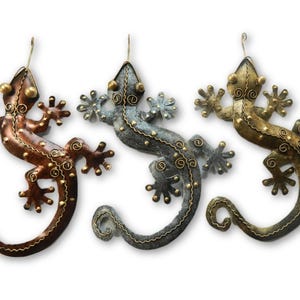 May include: Three metal gecko wall decor pieces in different colours: copper, silver, and gold. Each gecko has a detailed design with gold accents.