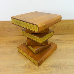 May include: A wooden side table shaped like a stack of books with gold accents. The table is made of dark wood and has a rustic look.