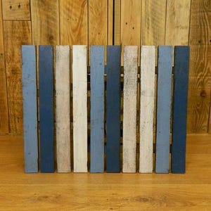 May include: A wooden panel made of multiple slats painted in shades of blue, white, and grey. The slats are arranged vertically and create a rustic, farmhouse-style design.