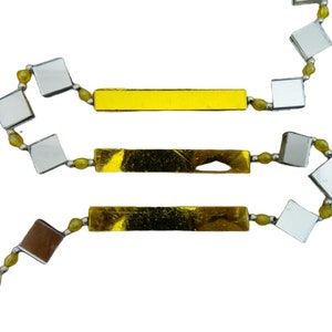 May include: A gold and silver decorative garland with three gold bars and a ring at one end. The garland is made of small square mirrors and yellow beads.