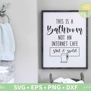 Pode incluir: Uma placa de casa de banho emoldurada com o texto "THIS IS A BATHROOM NOT AN INTERNET CAFE shit & split" em letras pretas. Uma toalha azul clara pendurada num porta-toalhas prateado. Uma cesta com toalhas brancas está por baixo.