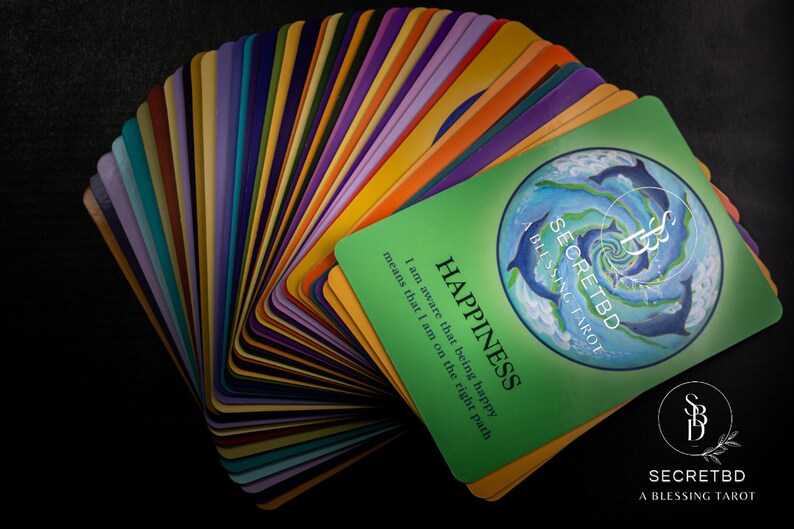 May include: A deck of colorful tarot cards with a green card on top that reads "SECRETBD A BLESSING TAROT" and "HAPPINESS I am aware that being happy means that I am on the right path".