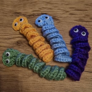 May include: Four crocheted worm toys with googly eyes. The worms are green, yellow, blue, and purple.