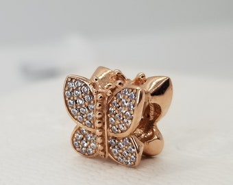 Puede incluir: Un charm de mariposa de oro rosa con piedras de circonita cúbica transparentes. El charm está diseñado para ser usado en una pulsera o un collar.