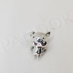 May include: A silver charm in the shape of a pig with wings. The pig has a small snout and large ears.