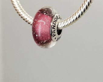 May include: A silver charm bracelet with a pink and white glass charm that says "Pandora" on it.