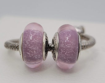 May include: Two purple glass beads with silver accents. The beads have a sparkly, speckled effect.
