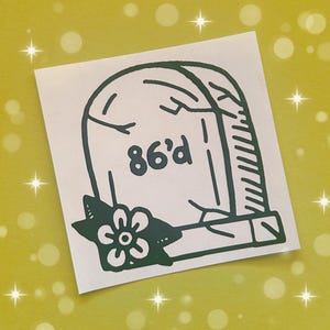 May include: A green sticker with a tombstone design. The tombstone has the words "86'd" written on it. A green flower with white petals is at the bottom of the tombstone.