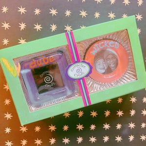 May include: A boxed set of "Computer Candy" with two items. One is a square, purple-tinted item with the word "dude" and "Computer Candy" on it. The other is an orange circle with a photo and the word "Wicked". The box is green.