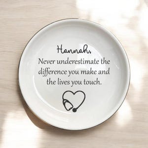 May include: White ceramic plate with a black rim. The plate features the name "Hannah," along with the text "Never underestimate the difference you make and the lives you touch." A heart-shaped stethoscope graphic is also present.