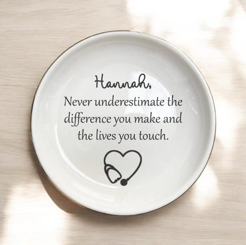 May include: White ceramic plate with a black rim. The plate features the name "Hannah," along with the text "Never underestimate the difference you make and the lives you touch." A heart-shaped stethoscope graphic is also present.
