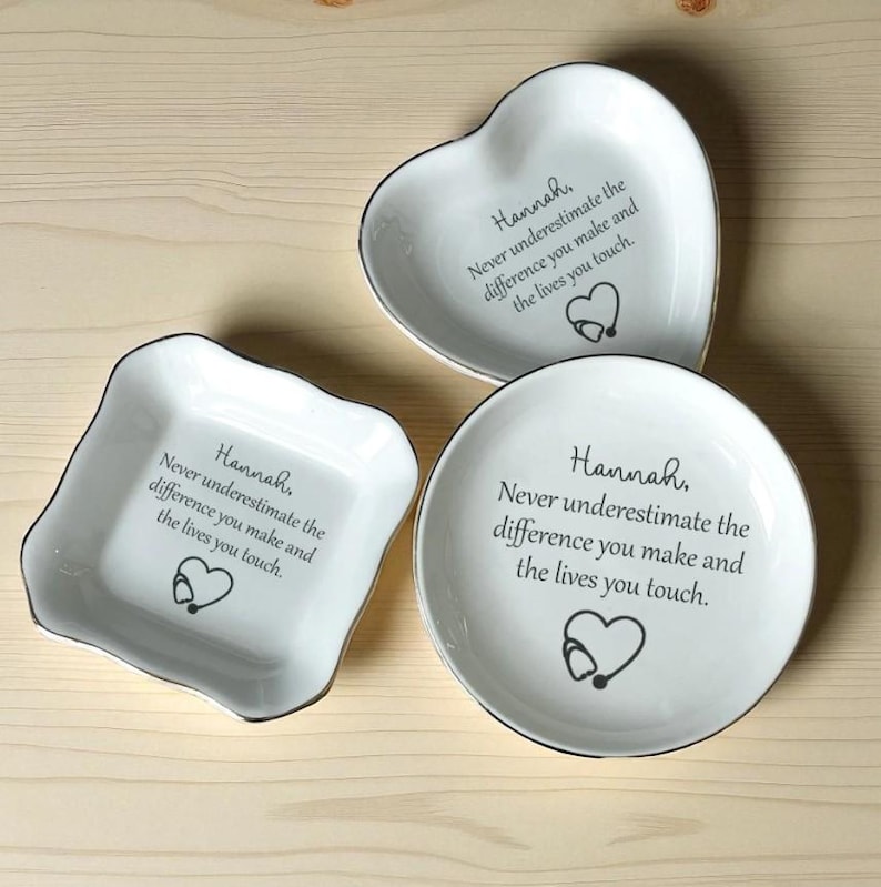 May include: Three white ceramic dishes in heart, square, and round shapes. Each dish has a black rim and features the text "Hannah, Never underestimate the difference you make and the lives you touch." A stethoscope heart graphic is also present.