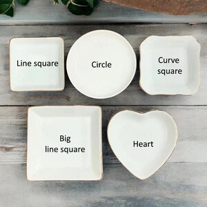 May include: A collection of white ceramic dishes in various shapes: square, round, and heart-shaped. Each dish has a gold rim and is labeled with its shape: "Line square", "Circle", "Curve square", "Big line square", and "Heart".