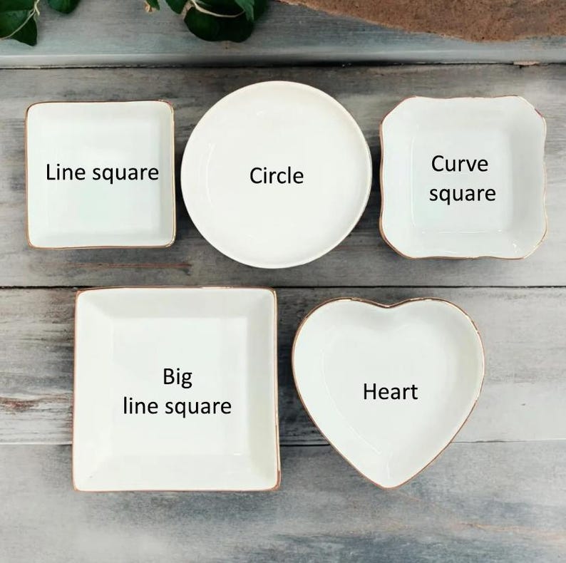 May include: A collection of white ceramic dishes in various shapes: square, round, and heart-shaped. Each dish has a gold rim and is labeled with its shape: "Line square", "Circle", "Curve square", "Big line square", and "Heart".