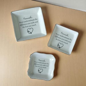 May include: Three white ceramic trinket dishes with silver trim. Each dish has the name "Hannah" and the text "Never underestimate the difference you make and the lives you touch." A heart and stethoscope graphic is also present.