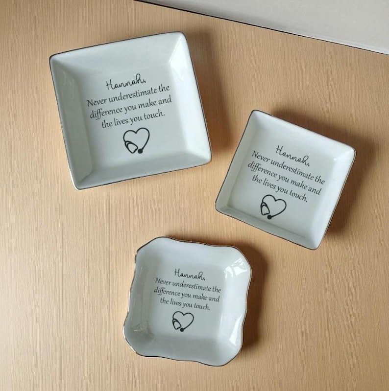 May include: Three white ceramic trinket dishes with silver trim. Each dish has the name "Hannah" and the text "Never underestimate the difference you make and the lives you touch." A heart and stethoscope graphic is also present.