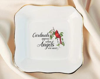 May include: White square trinket dish with a gold rim. The dish features a red cardinal bird perched on a flowering branch. Text on the dish reads "Cardinals appear when Angels are near."
