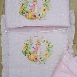May include: Pink baby bedding set featuring a floral and bunny design. The set includes a pillow, a blanket, and a fitted sheet.