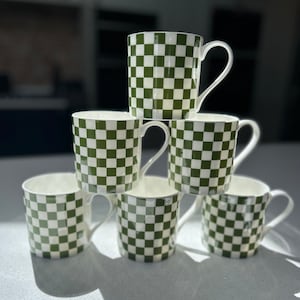 Może przedstawiać: Sześć białych ceramicznych kubków z zielono-białym wzorem w kratkę. Kubki są ułożone w kształcie piramidy.