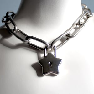 May include: A silver chain necklace with a star-shaped padlock pendant.