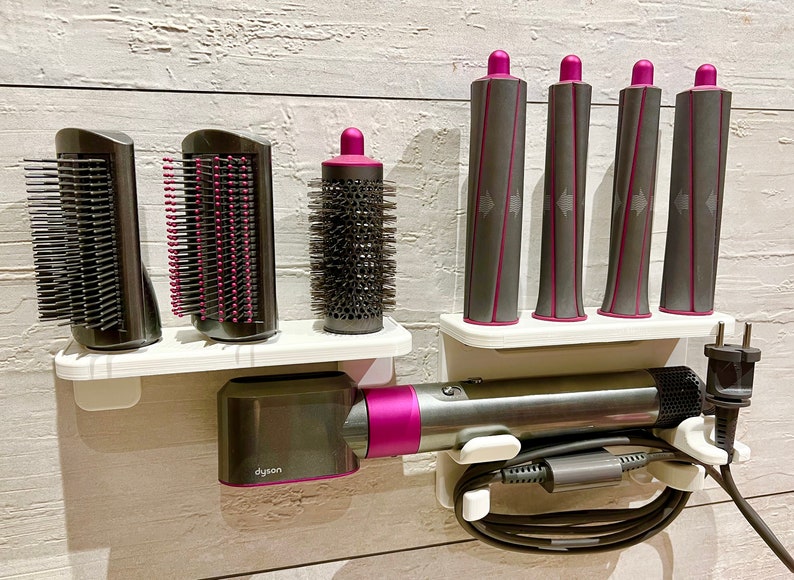 May include: A white wall-mounted organizer with a Dyson hair dryer, a round brush attachment, and four curling iron attachments. The organizer has a white shelf and a gray cord holder.
