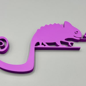 May include: A purple 3D printed chameleon figurine with a curled tail. The chameleon is holding a leaf in its mouth.