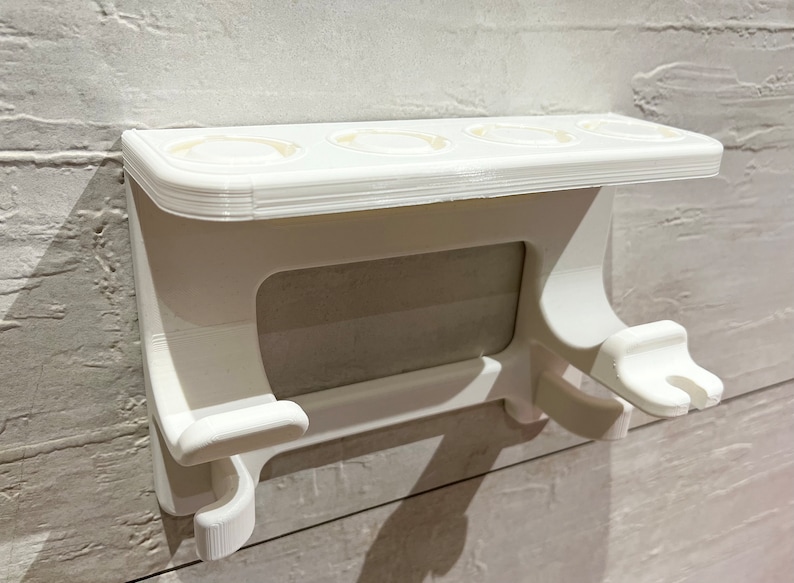 May include: White plastic toothbrush holder with four toothbrush slots and two hooks for hanging items. The holder is mounted on a wall.