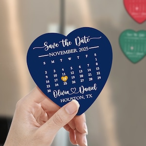 Könnte beinhalten: Ein blauer herzförmiger Save-the-Date-Magnet mit einem Kalender für November 2025. Das Datum 18 ist in Gold hervorgehoben. Der Text "Save the Date - November 2025" und "Oliwia & Daniel HOUSTON, TX" ist auf dem Magneten gedruckt.