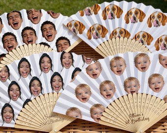 May include: Several personalized paper fans with various faces printed on them, including a smiling young man, a smiling young woman, a baby, and a dog. The fans are in a woven basket.