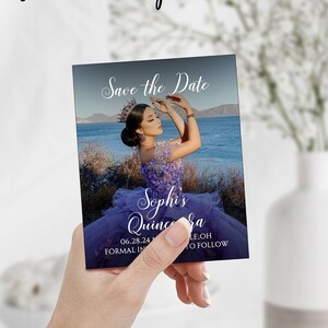 May include: Save the Date card for a Quincea&ntilde;era with a photo of a young woman in a purple dress. The card has a blue background with a photo of a lake and mountains in the background. The text on the card reads "Save the Date", "Sophis Quincea&ntilde;era", "06.28.24", "Formal Invitations to Follow".