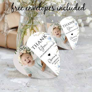 May include: Heart-shaped thank you cards featuring a baby's photo, floral details, and the words "Thank You." The cards are personalised with "Olivia's" and the date "1st Birthday May 14.26." The text "free envelopes included" is written at the top.