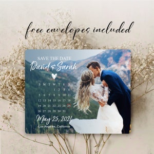 May include: Save the date card with a photo of a couple kissing in front of a mountain range. The card features a calendar with the date May 25, 2024 circled in red. The text "David & Sarah" is written in white script with a heart symbol.