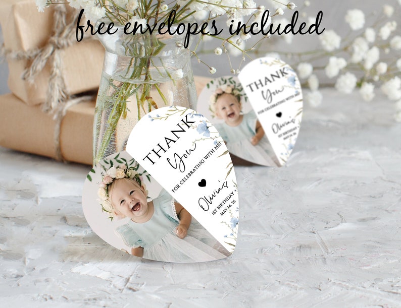 May include: Heart-shaped thank you cards featuring a baby's photo, floral details, and the words "Thank You." The cards are personalised with "Olivia's" and the date "1st Birthday May 14.26." The text "free envelopes included" is written at the top.