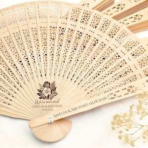 May include: A wooden hand fan with a floral design and the text "We're married Amelia & Michael 05.18.2026" engraved on the handle.