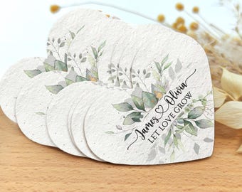 May include: Heart-shaped seed paper with watercolor floral design. The paper features green leaves and the text "James & Olivia LET LOVE GROW". The paper is white with a textured surface.