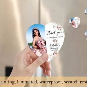 May include: Heart-shaped thank you magnet with a photo of a young woman in a quincea&ntilde;era dress. The magnet has a floral design and the text "Thank you for making this day so special! Isabella's Quincea&ntilde;era 08.17.2025".