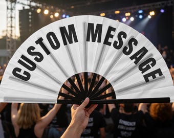 Op de afbeelding: Een witte opvouwbare handwaaier met zwarte plastic baleinen en de tekst CUSTOM MESSAGE in dikke zwarte hoofdletters op het stoffen oppervlak. De waaier is volledig uitgevouwen in een halve cirkel en toont de duidelijke tekst.