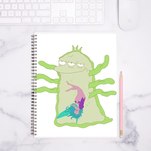 May include: Spiral-bound notebook featuring a cartoon illustration of a green, blob-like creature with multiple arms, containing a smaller figure inside. The smaller figure has blue hair and is wearing purple and pink clothing. A pink pencil rests on the right.