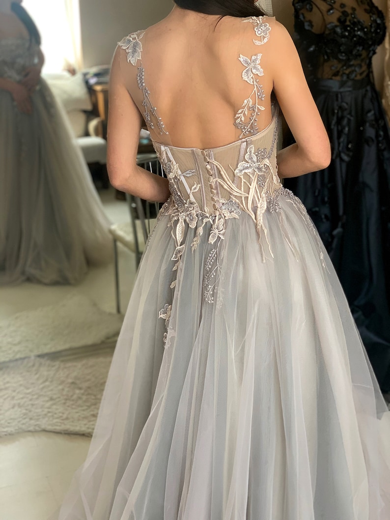 May include: A light grey tulle gown with delicate floral embroidery and a sheer bodice. The gown has a fitted bodice and a flowing skirt.