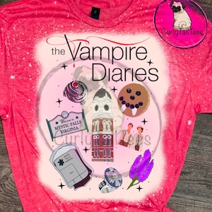 May include: A red t-shirt with a graphic design featuring elements from "The Vampire Diaries." The design includes the show's title, a clock tower, a sign that says "Welcome to Mystic Falls Virginia," and other related illustrations. The shirt has a bleached effect.